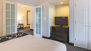 Une chambre d’hôtel avec un lit, un téléviseur posé sur une commode et une porte donnant sur une autre pièce.