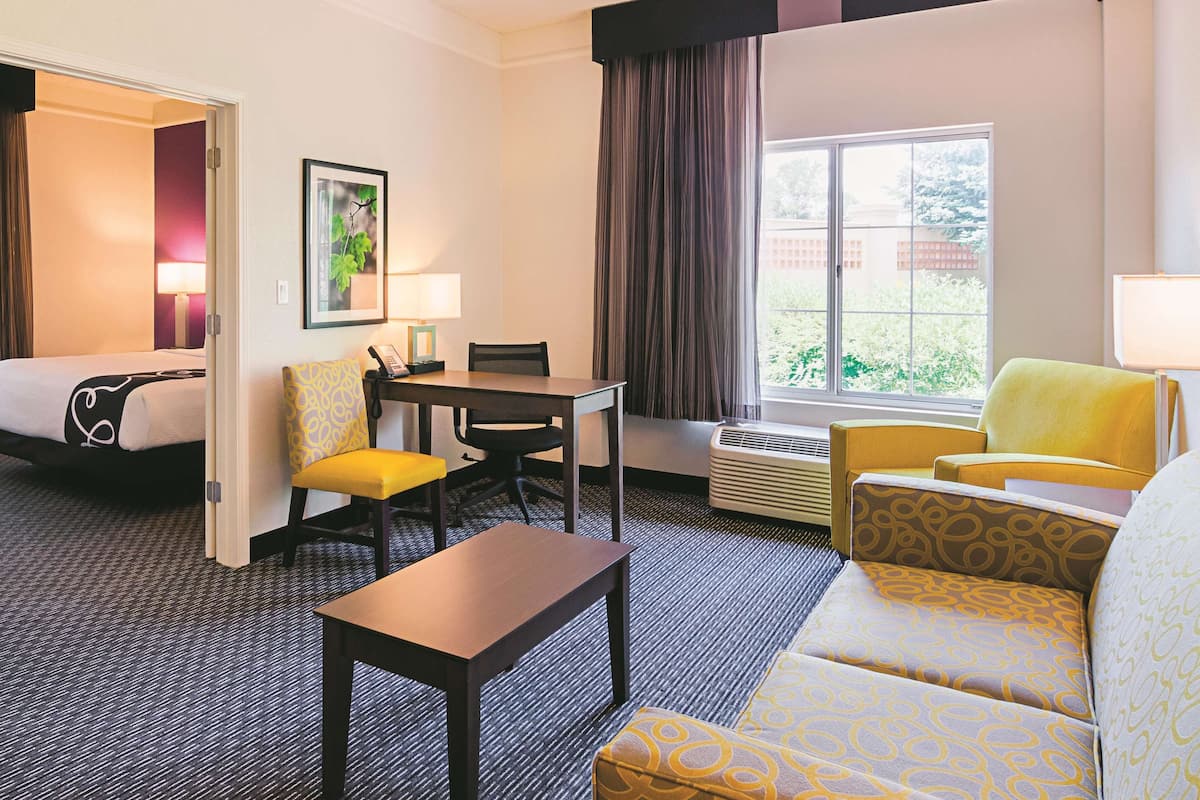 Una habitación de hotel con cama, escritorio, sillón, sofá y ventana con cortinas.
