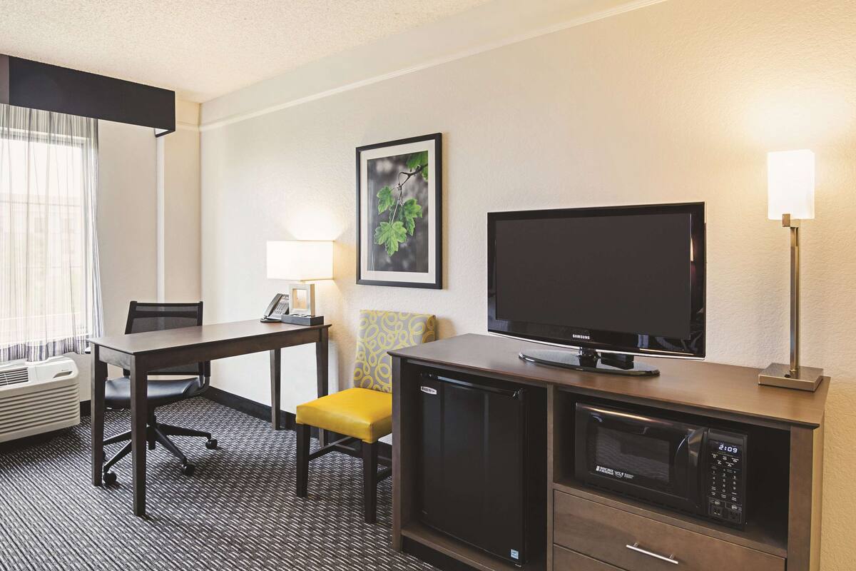Una habitación de hotel con escritorio, silla, televisión, microondas y un pequeño armario.