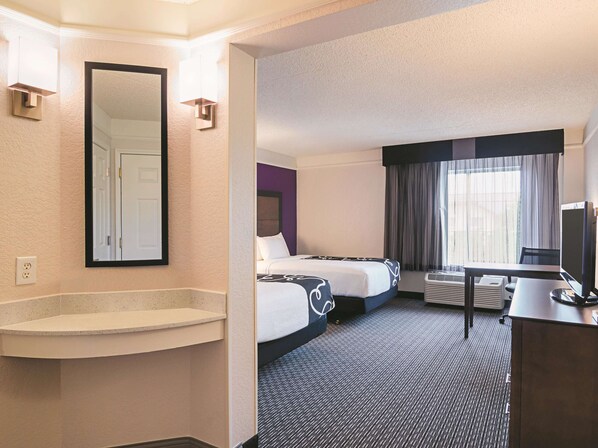 A hotel room with a large mirror, a bed, a desk, and a window with curtains.