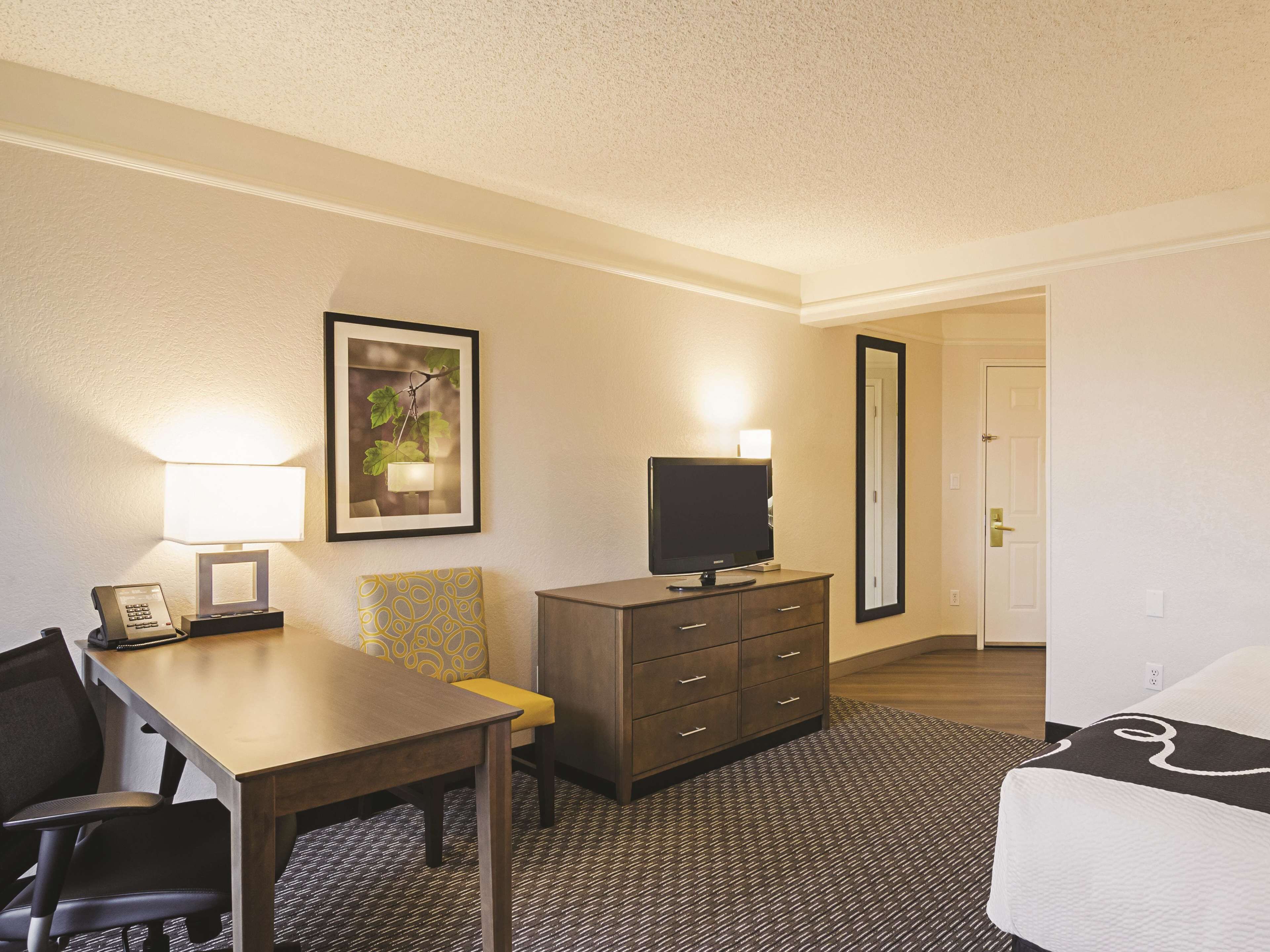 A hotel room with a desk, chair, television, dresser, and a bed.
