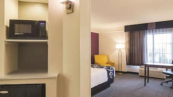 A hotel room with a bed, a desk, a chair, a microwave, a lamp, and a window with curtains.