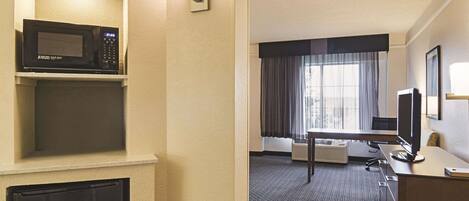 A hotel room with a microwave, refrigerator, desk, and a large window with curtains.