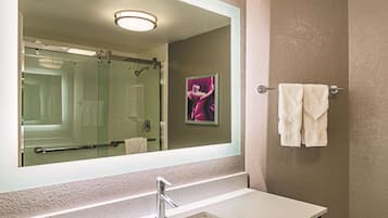 Un baño con un espejo grande, un lavabo, un perchero para toallas y una ducha.
