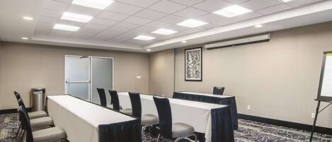 A conference room with a long table, chairs, a projector screen, and a carpeted floor.