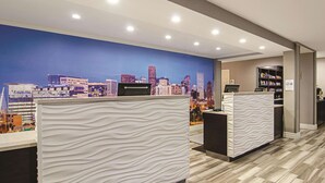 Un espace d’accueil d’hôtel au design moderne, comprenant une fresque représentant un paysage urbain, des comptoirs d’accueil et un bar servant des collations.