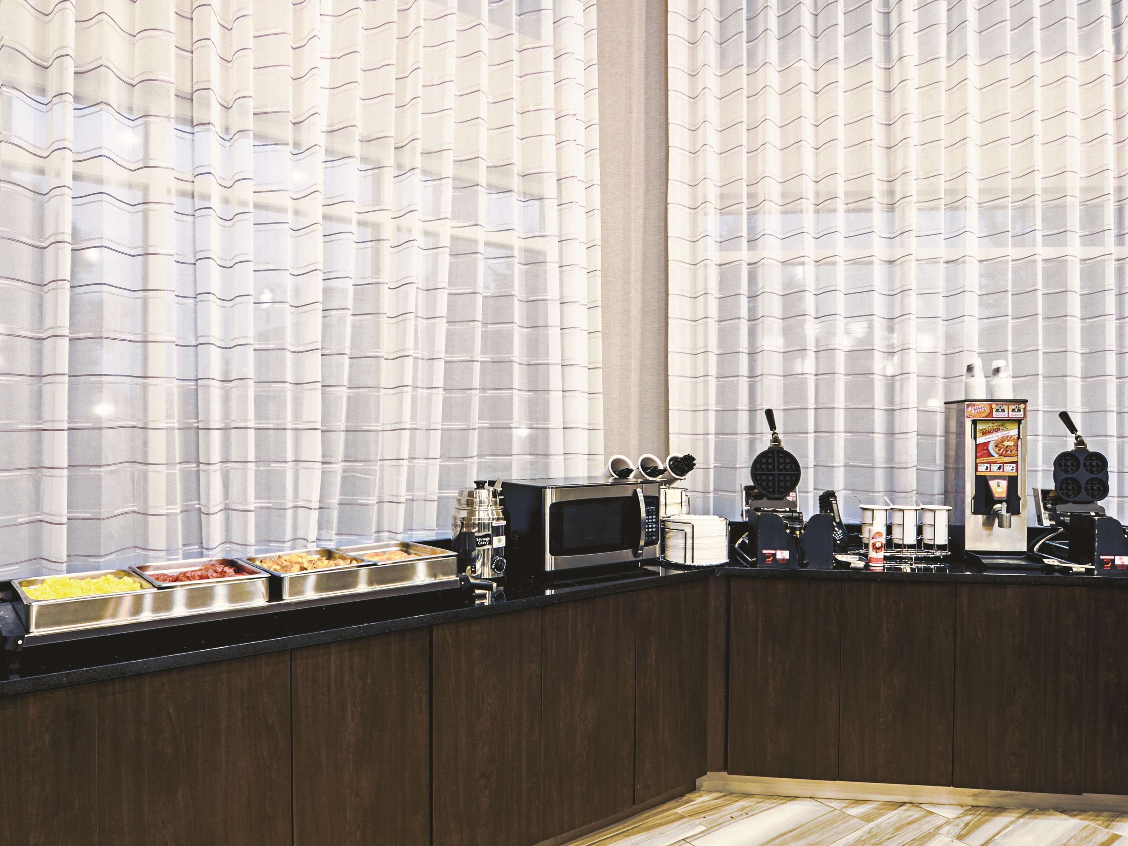 A breakfast bar with a waffle maker, coffee machine, and a beverage dispenser.