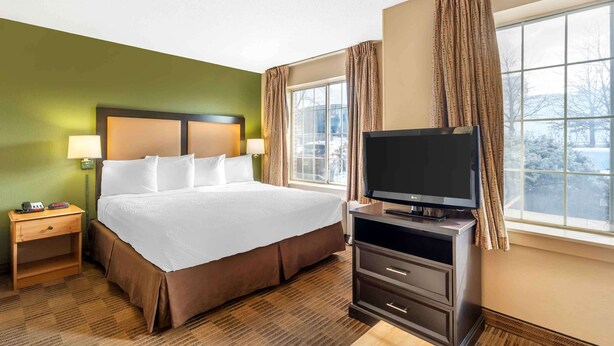 A hotel room with a large bed, a TV on a stand, a nightstand, and a window with curtains.