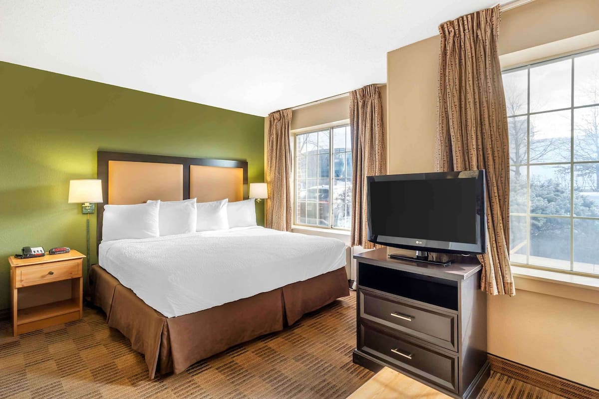 Une chambre d’hôtel avec un grand lit, un téléviseur posé sur un meuble, une table de chevet et une fenêtre avec des rideaux.