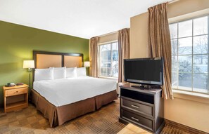 A hotel room with a large bed, a TV on a stand, a nightstand, and a window with curtains. - Extended Stay America Select Suites Chicago Westmont Oak Brook (Westmont)