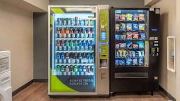 Two vending machines in a hallway, one with a variety of beverages and the other with snacks.