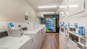 A laundry facility with multiple washing machines and dryers, a vending machine, and a sign indicating the location.