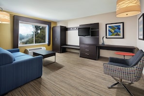 A modern hotel room with a sofa, a desk, a television, and a view of the outdoors. - Holiday Inn Express Suites Belmont by IHG (Belmont)