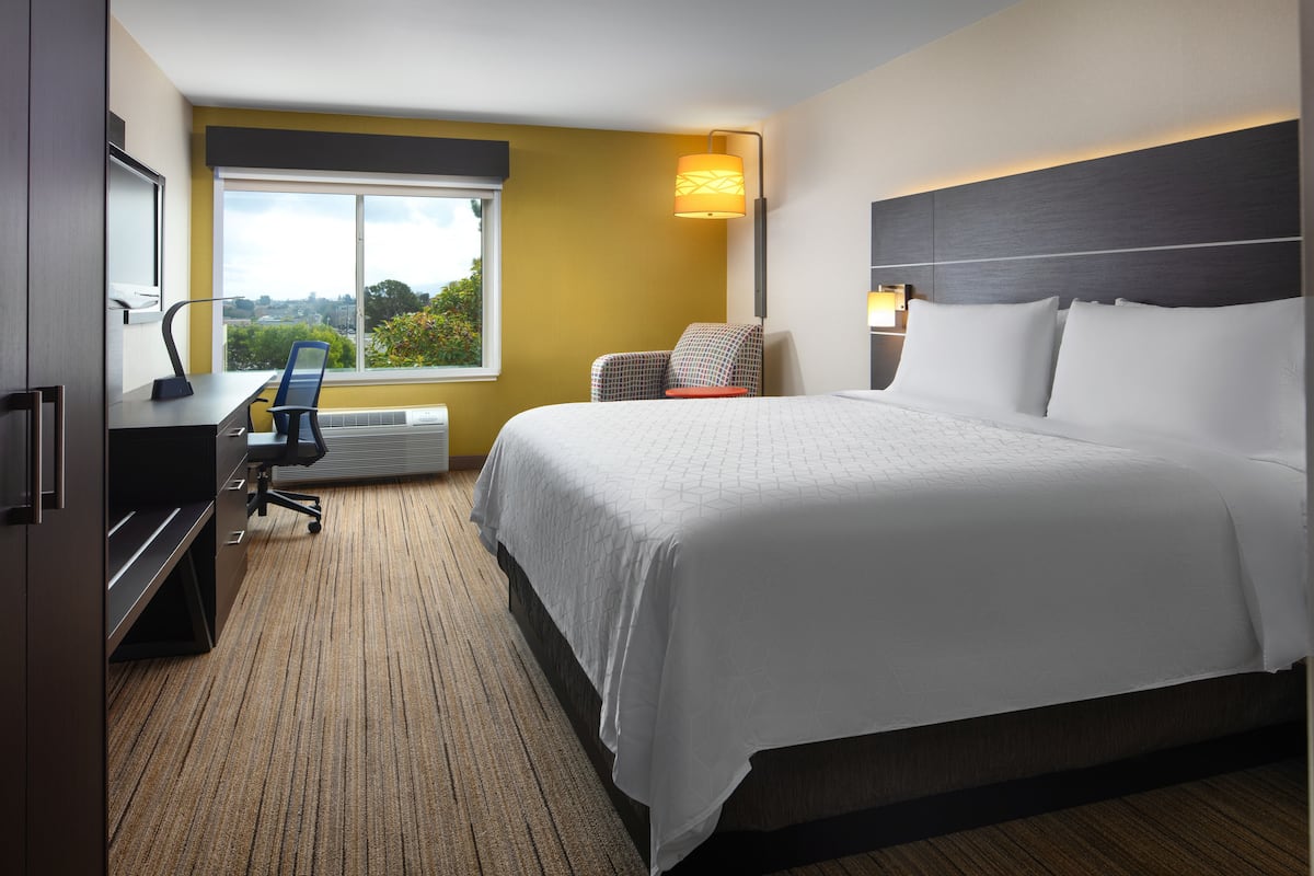 A hotel room with a large bed, a desk with a chair, a TV, and a window with a view of the outdoors.