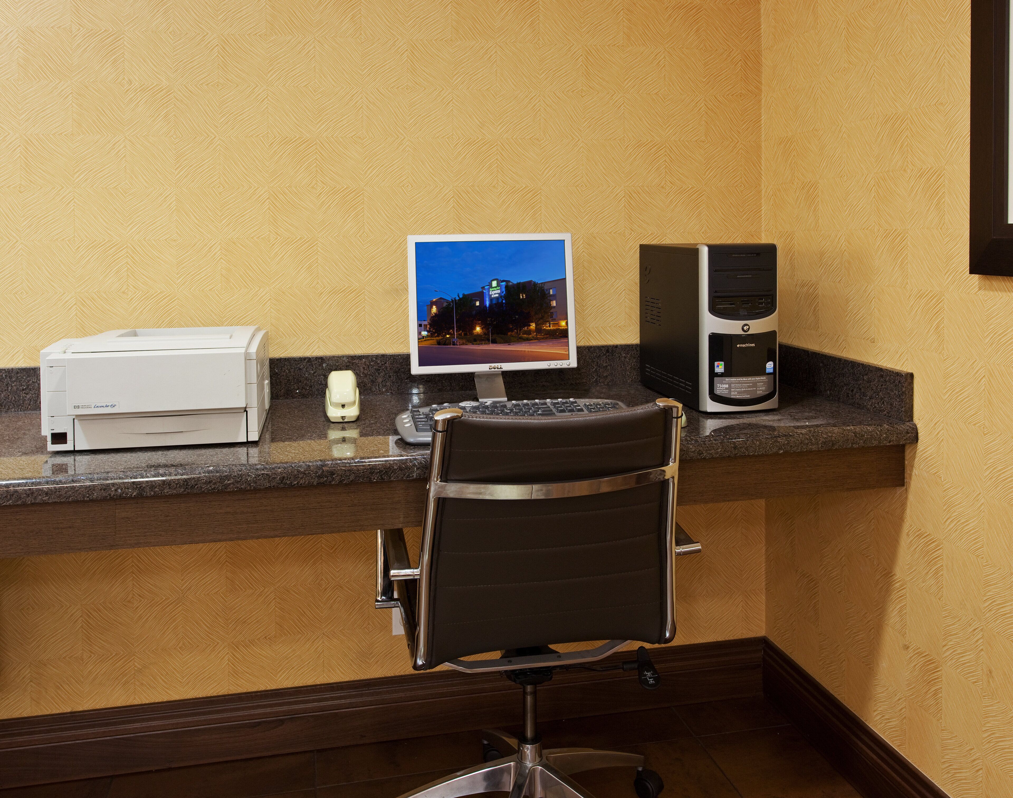 A hotel reception desk with a desktop computer, a printer, and a chair.