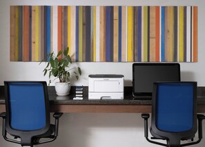 A workspace with two blue office chairs, a printer, a laptop, a potted plant, and a colorful striped wall art. - Holiday Inn Express Suites Belmont by IHG (Belmont)