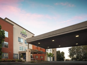 A hotel with a covered entrance, multiple windows, and a stone pillar. - Holiday Inn Express Suites Belmont by IHG (Belmont)
