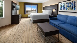A hotel room with a bed, a TV, a sofa, and a large window with a city view. - Holiday Inn Express Suites Belmont by IHG (Belmont)