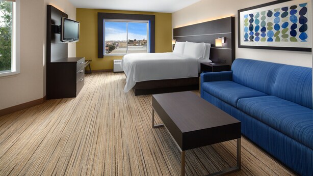 A hotel room with a bed, a TV, a sofa, and a large window with a city view.