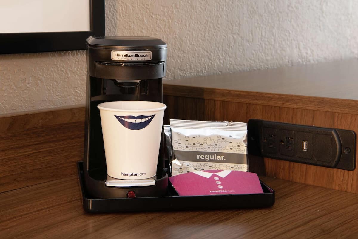 A Hamilton Beach commercial coffee maker with a cup and a packet of coffee pods on a tray.