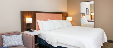 A hotel room with a bed, a bedside table with a phone, a chair, and a mirror.