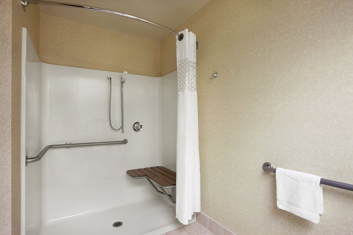 A shower area with a grab bar, a shower seat, and a towel rack.