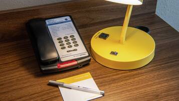 A hotel room with a desk, a telephone, a lamp, and a notepad.