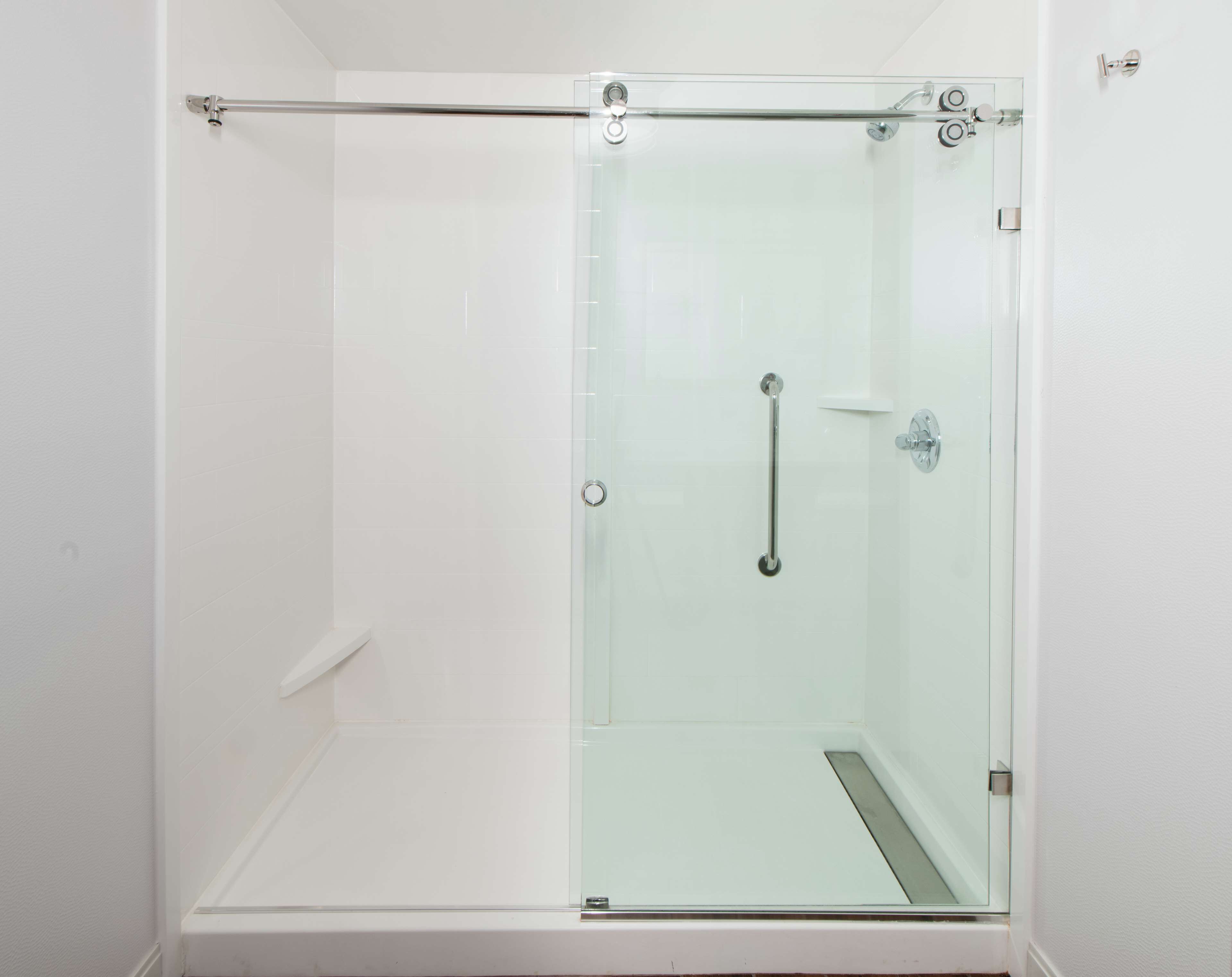 A glass-enclosed shower with a handrail, a door with a handle, and a white tiled wall.