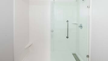 A glass-enclosed shower with a handrail, a door with a handle, and a white tiled wall.