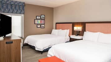 A hotel room with two beds, a TV, a desk, and a wall with framed pictures.