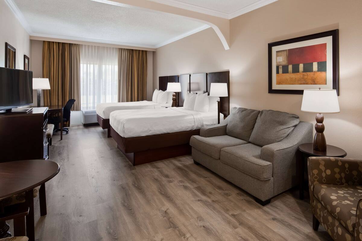 Une chambre d’hôtel avec deux lits, un canapé, un bureau, une télévision et un tableau au mur.