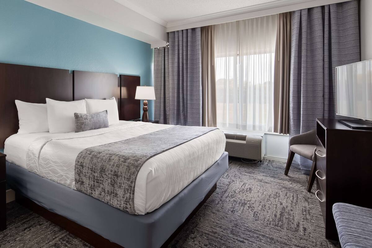 Une chambre d’hôtel avec un grand lit, des tables de chevet, un bureau avec une chaise, une télévision et une fenêtre avec des rideaux.