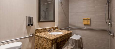 A modern bathroom with a granite sink, a mirror, a handheld showerhead, and a grab bar.