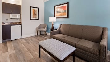 Una sala de estar con un sofá marrón, un reposapiés a rayas, una mesita, una lámpara y una obra de arte enmarcada en la pared.