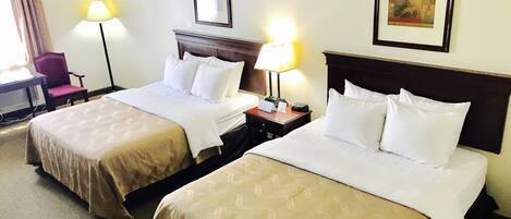 A hotel room with two beds, a desk, a chair, and a lamp.