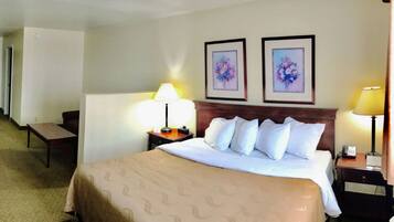 A hotel room with a bed, two bedside tables with lamps, a chair, and two framed floral paintings on the wall.