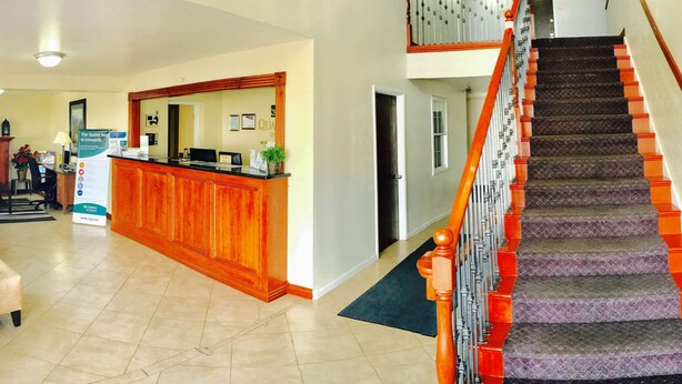 A reception area with a wooden counter, a staircase with red and black carpeting, and a tiled floor.