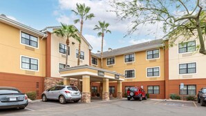 A multi-story hotel with a lobby entrance, parking lot, and palm trees.