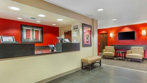A hotel reception area with a counter, a bench, two armchairs, a television, and a wall-mounted sign.