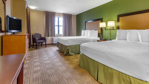 A hotel room with two beds, a desk, a chair, a television, and a window with curtains.