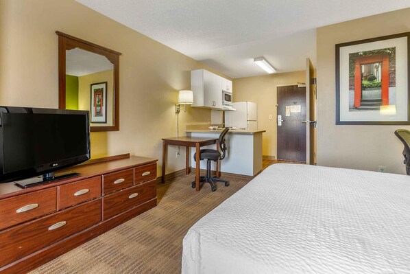 A hotel room with a bed, a TV, a desk with a chair, a microwave, and a door leading to another room.