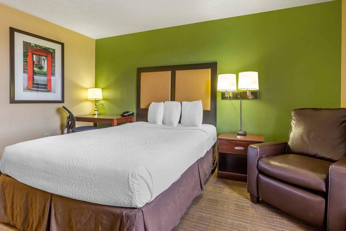 A hotel room with a large bed, two bedside tables, a brown leather chair, and a green accent wall.