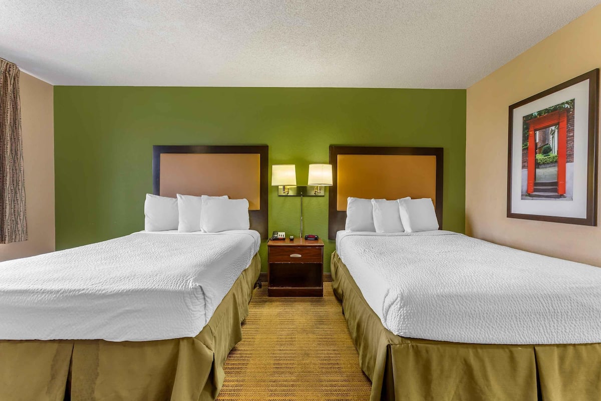 A hotel room with two beds, a nightstand with lamps, and a framed picture on the wall.