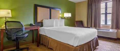 Een hotelkamer met een bed, bureau, bureaustoel, lampen en een airconditioning.
