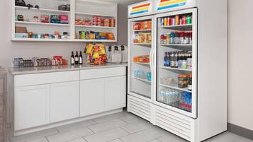Una cocina con armarios blancos, una encimera con aperitivos y un refrigerador lleno de bebidas.