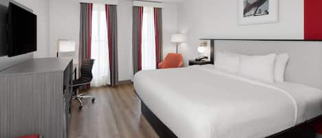 A hotel room with a large bed, a desk with a flat-screen TV, a chair, and a lamp.