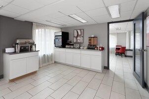A modern kitchen with a built-in stove, refrigerator, and coffee machine. There is a dining area with a red chair and a table.