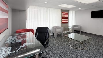A modern office space with a glass table, black and white chairs, and a large screen on the wall.