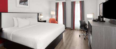 Una habitación de hotel moderna con una cama grande, un escritorio con silla, televisor y ventana con cortinas.