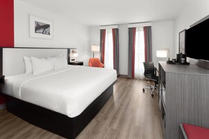 A modern hotel room with a large bed, a desk with a chair, a television, and a window with curtains.
